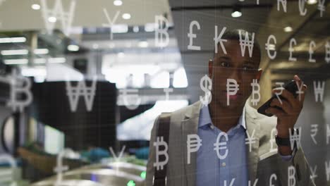 animation of currency symbols against african american businessman talking on smartphone at office