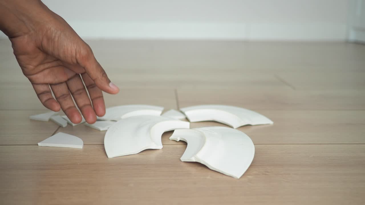 Broken Plate on Floor with Hand Picking Up Pieces