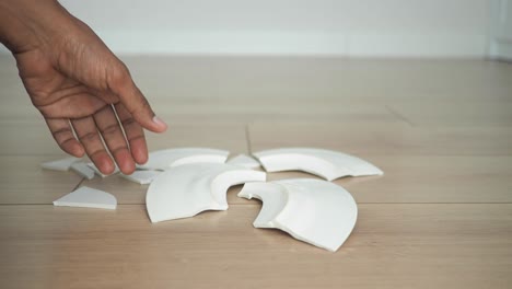 broken plate on floor with hand picking up pieces