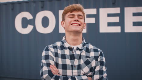 portrait of smiling male intern at freight haulage business standing by shipping container