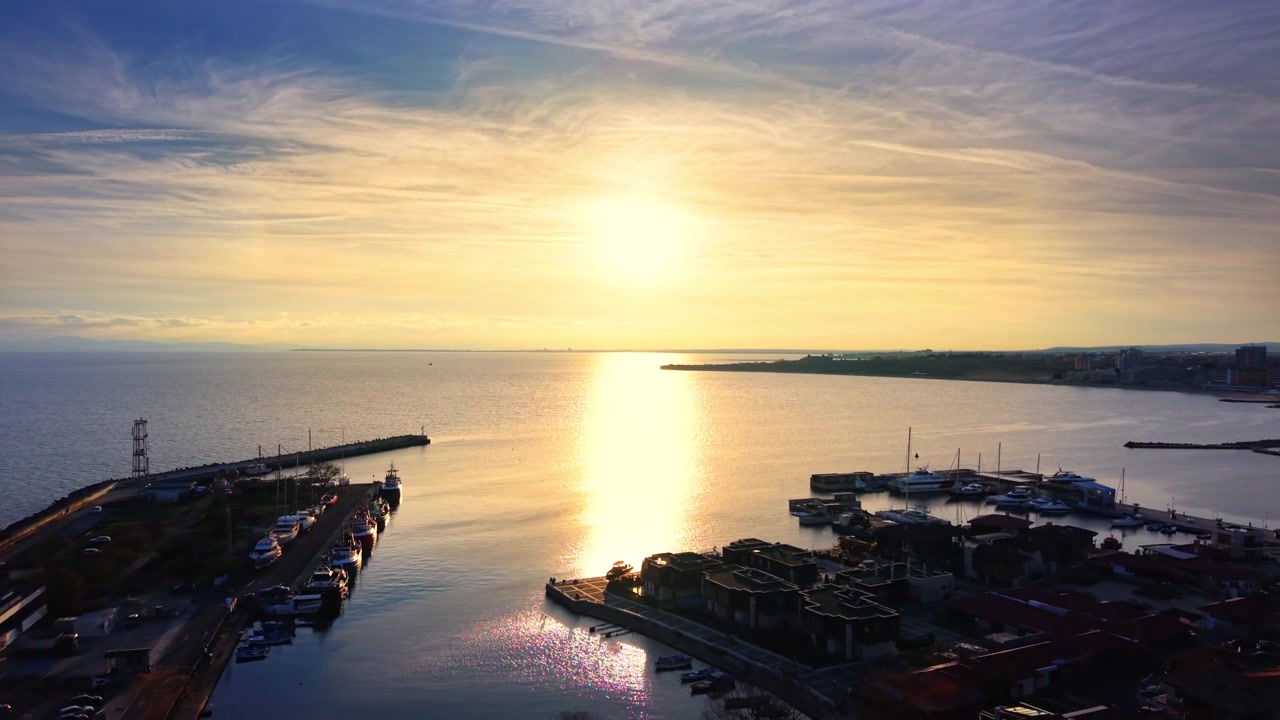 Drönarvy över en marina vid solnedgången, Bulgarien. Båt förtöjd längs vågbrytaren med solen som reflekteras över en lugn vik och avlägsen kustlinje.