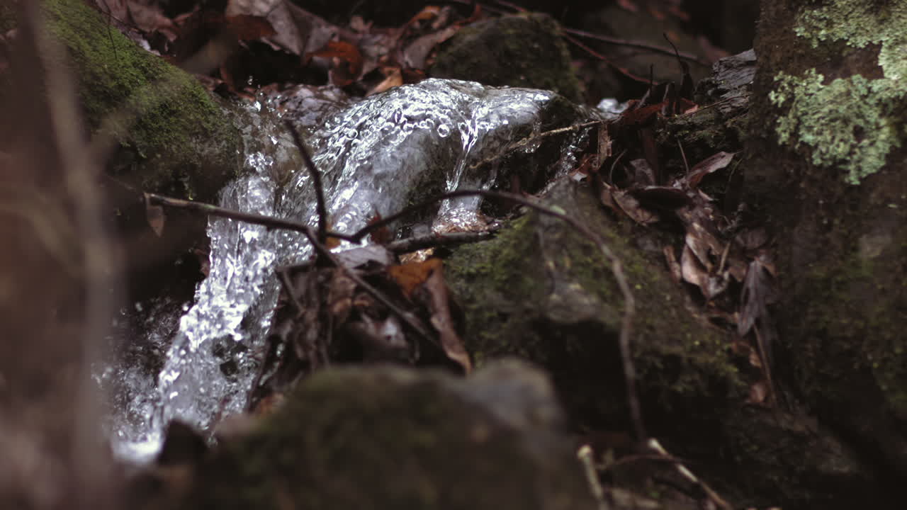 Super slow motion footage of a small stream falling over the rocks in the winter.