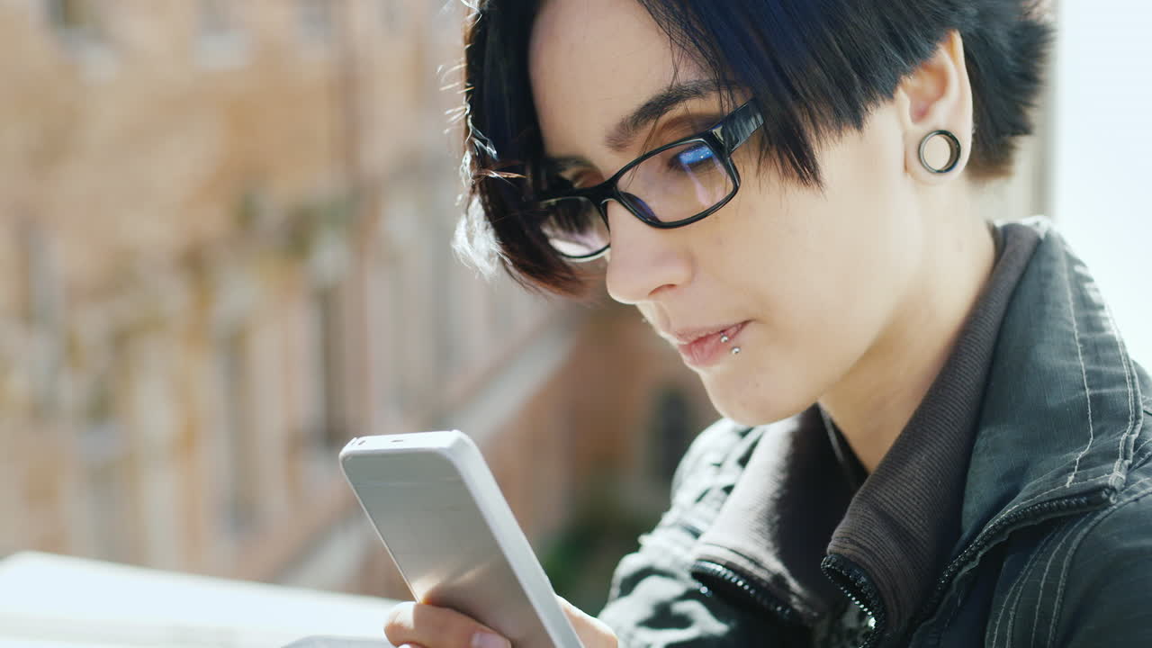 窓辺で携帯電話を使いながら夢想する、ヒップスター眼鏡をかけた若い女性の肖像。