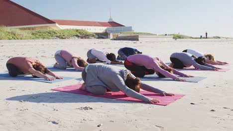 grupo multiétnico de mujeres haciendo posición de yoga en la playa y fondo de cielo azul