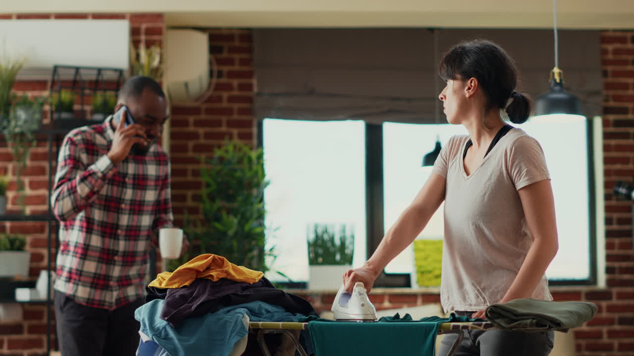 Young housewife ironing laundered clothes and feeling frustrated about doing chores alone