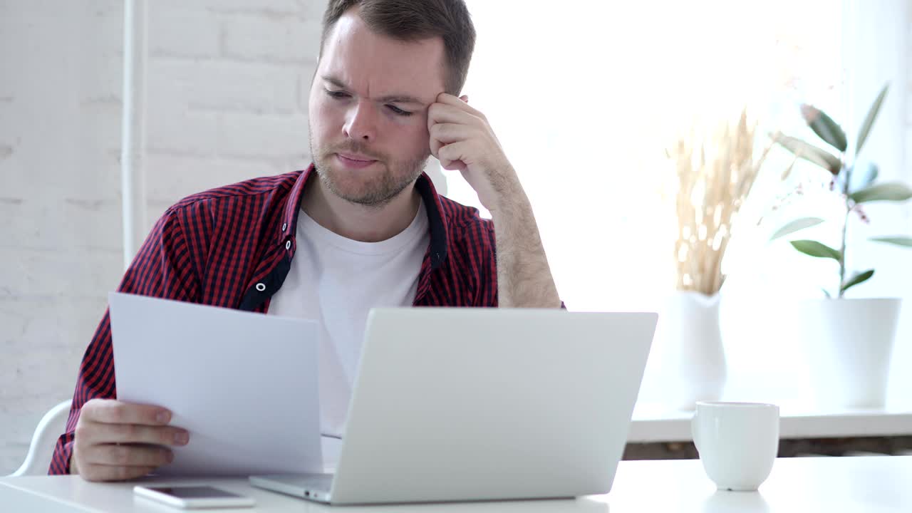 joven leyendo documentos y trabajando en una computadora portátil