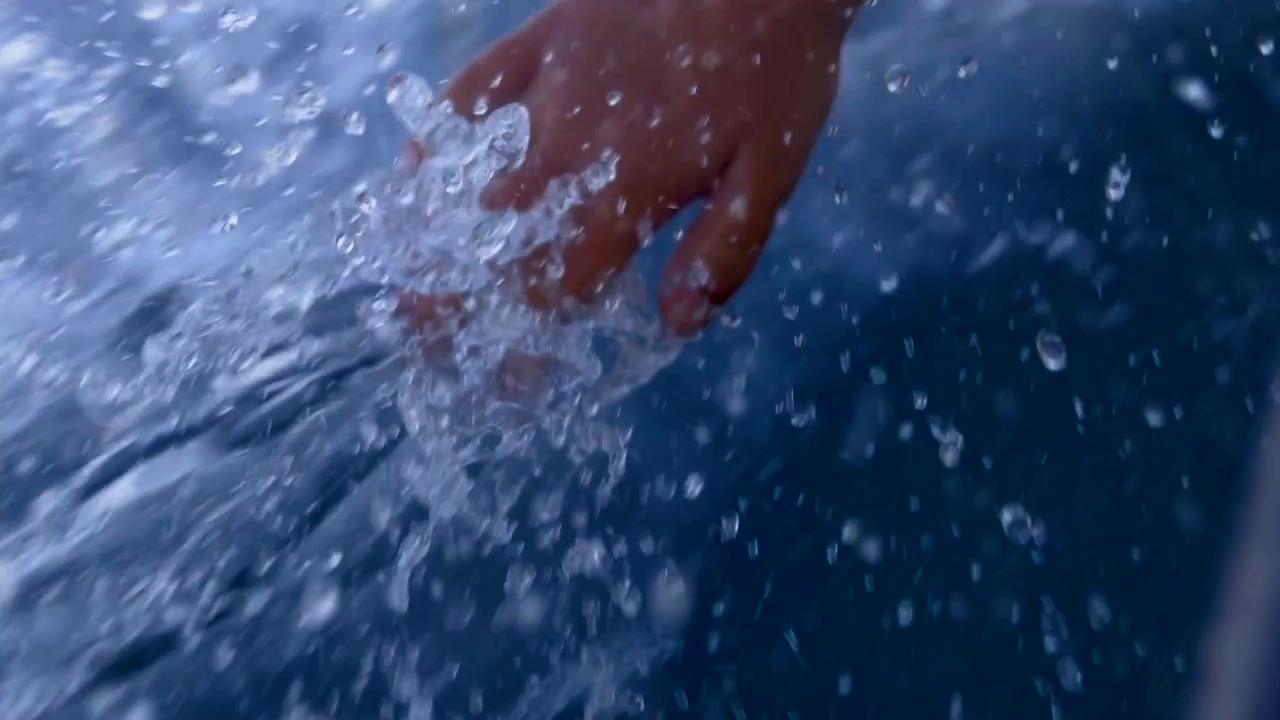 Toma a cámara lenta de la mano de un niño tocando el agua en movimiento mientras un pequeño barco pesquero navega en el Océano Atlántico en Portugal