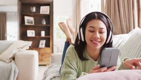 Video-of-smiling-biracial-woman-with-dark-hair-using-headphones-and-smartphone