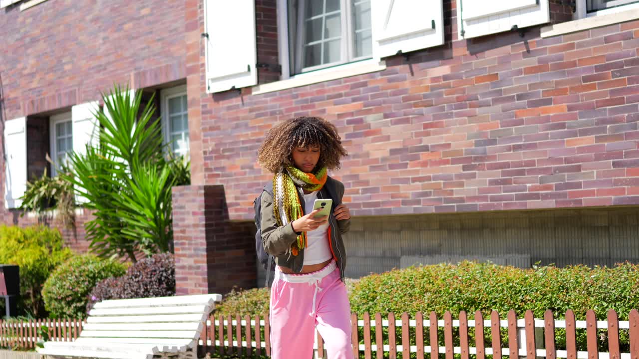 Young woman with curly hair walking near a brick building