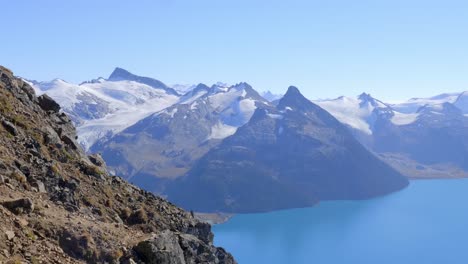 Snowy-Peak-Of-Mountain-Range-With-Calm-Lake-During-Summer