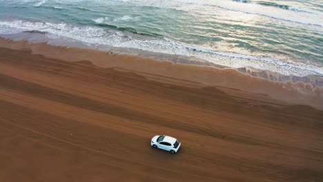 Sunset-over-Beach-as-Car-Drives-along-Seaside,-Aerial-Pan-Shot