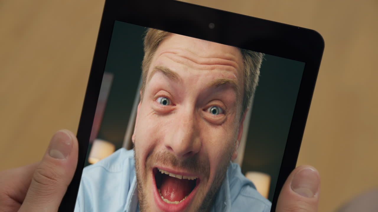 Primo piano di un uomo sorpreso che guarda lo schermo di una videochiamata su tablet in una stanza. Imprenditore che tiene in mano un computer