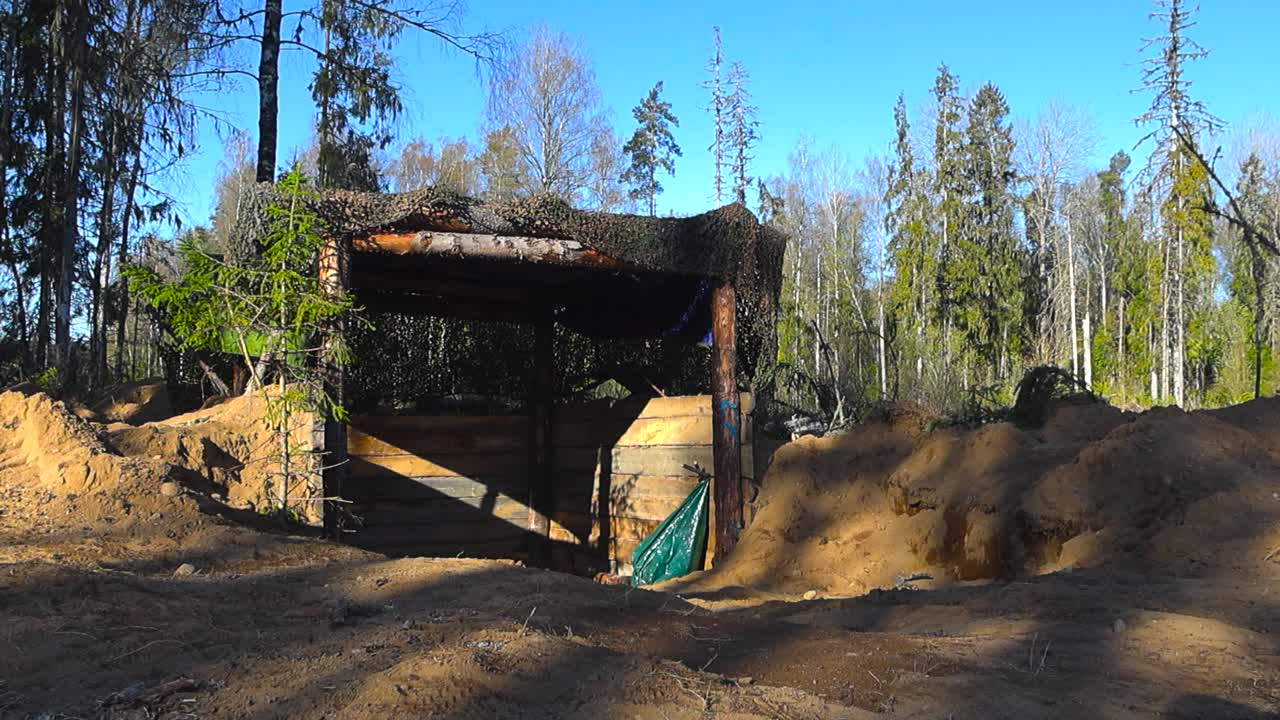 Rare footage of a army or military machine gun bunker hideout trench build out of sand and pine tree logs and disguised with camouflage green and brown net in a sunny pine forest during summer time.