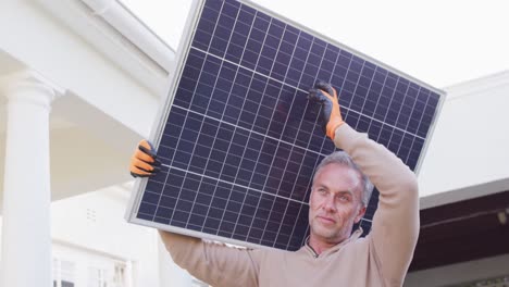 happy caucasian man wearing gloves, holding solar panel and walking