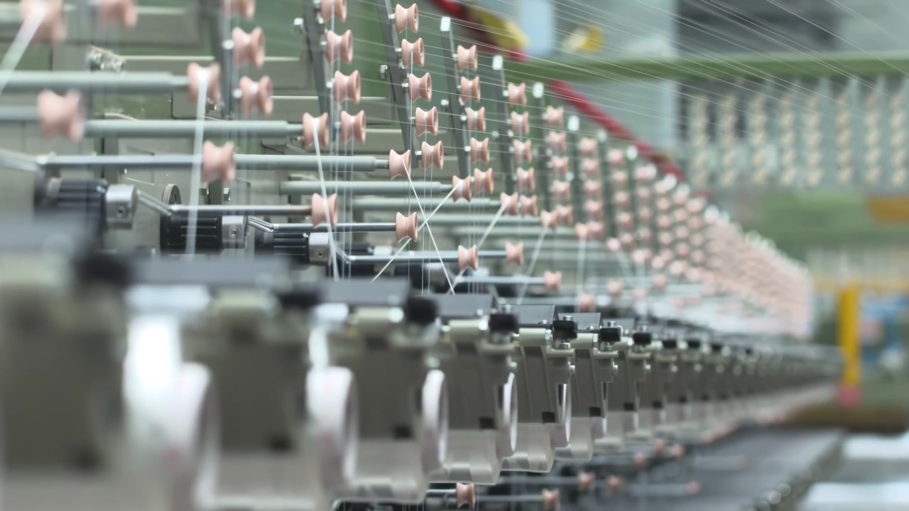 สายการผลิตในโรงงานอุตสาหกรรมอัตโนมัติที่กำลังทอเส้นด้ายโพลีโพรพิลีนสำหรับทำถุงและเครื่องปั่นด้ายสิ่งทอ ม้วนด้ายสีขาวพร้อมเชือกที่กำลังผลิตกระสอบพลาสติกหรือกระบวนการผลิตผ้าในโรงงานผลิตไนลอน