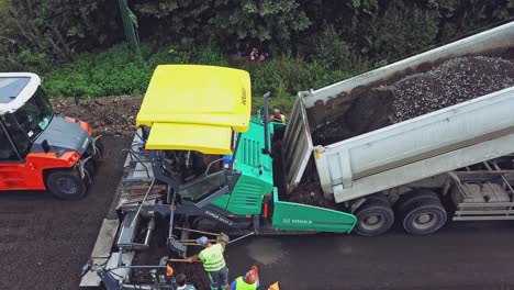 a process of laying asphalt by repairmen using an asphalt paver, a vibro-roller and a truck on a highway between cities. aerial view.