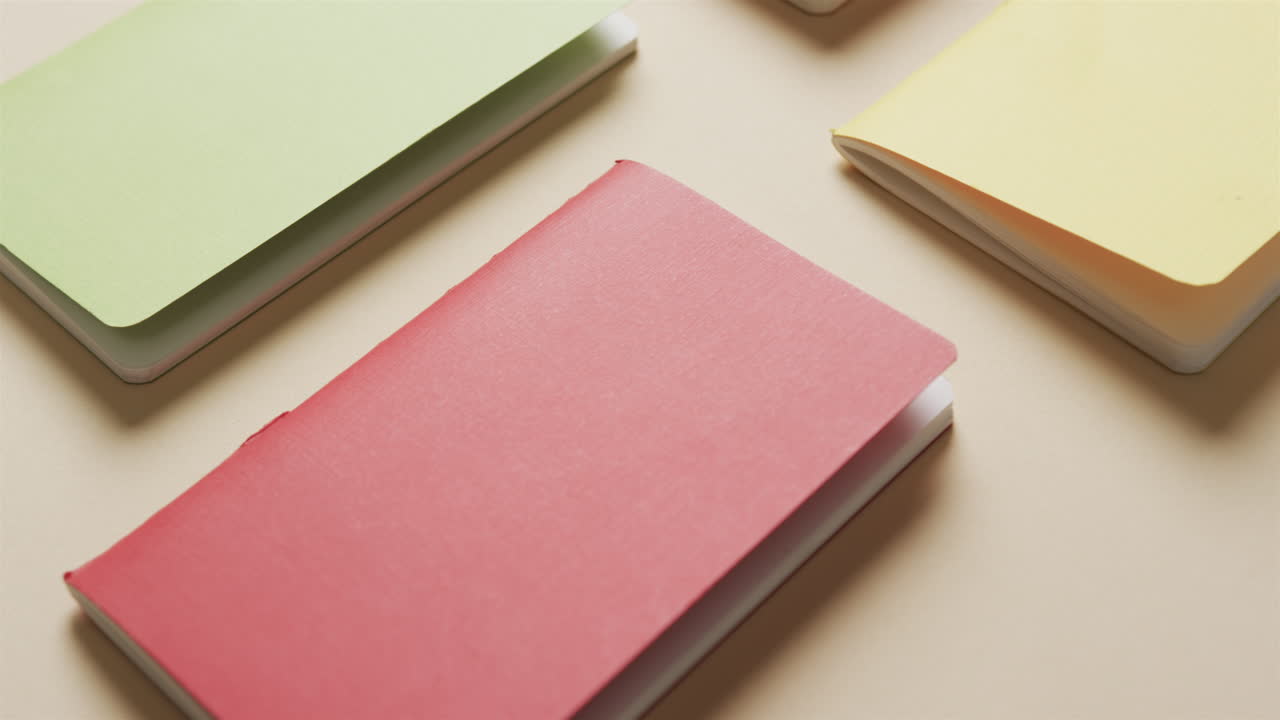 Close up of colourful notebooks arranged on beige background, in slow motion