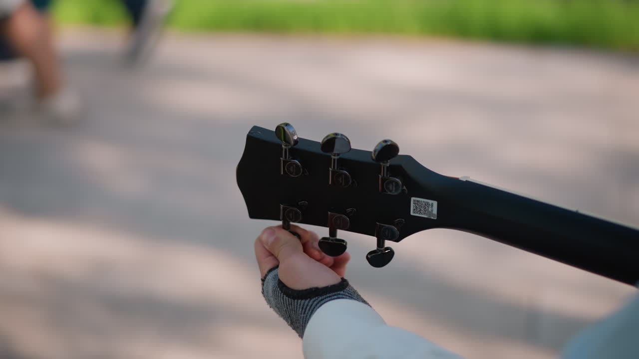 Gademusiker justerer guitarstrenge. Introspektiv musiker stemmer akustisk guitar udendørs. Ensom gadekunstner justerer omhyggeligt sin akustiske guitar på en parkbænk i blødt sollys