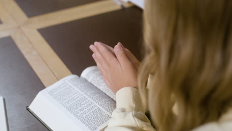 Chica-Rubia-Rezando-Con-Las-Manos-En-La-Biblia-En-Clase