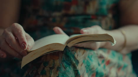 front view of senior woman turning page of a book while sitting and reading in her living room house