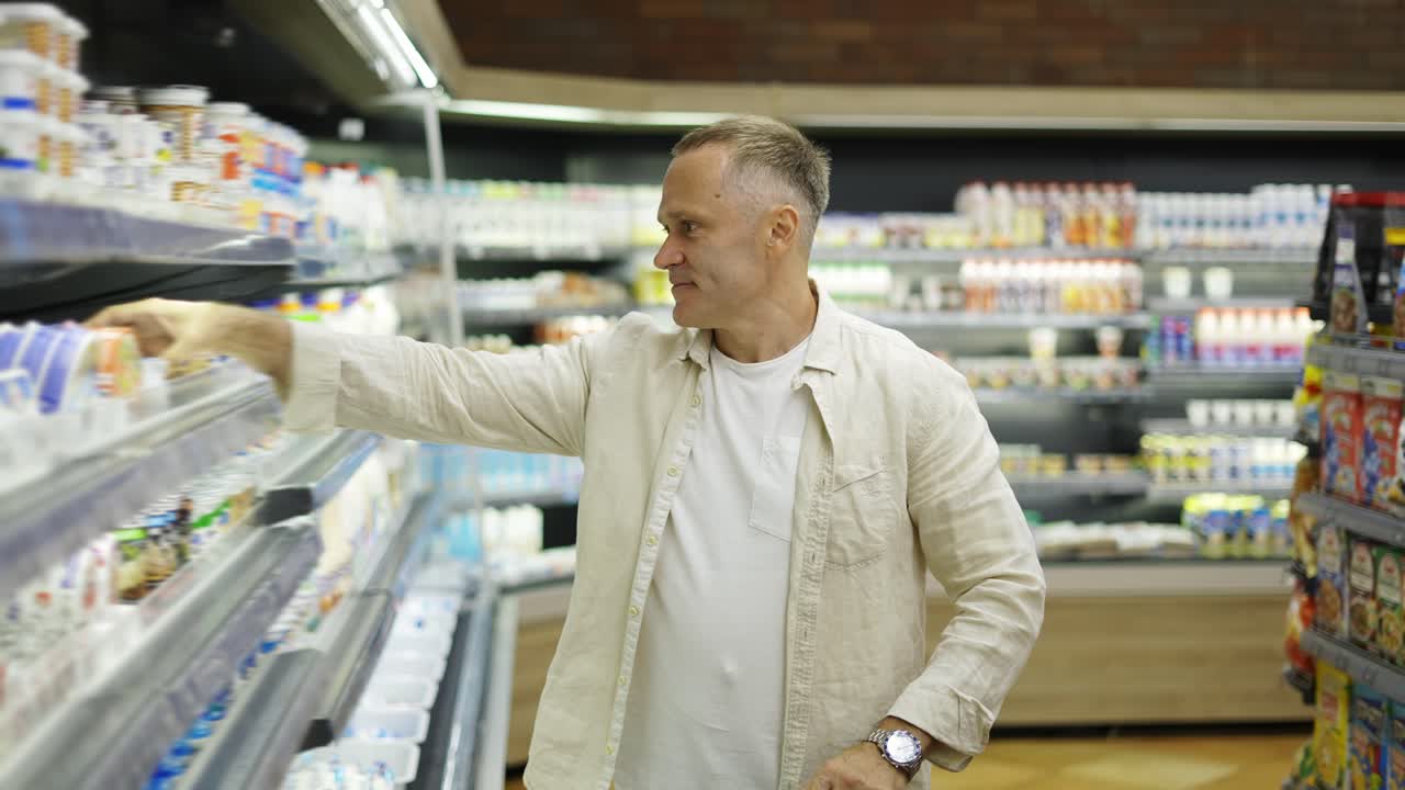 un visitante de mediana edad en una tienda de comestibles elige productos lácteos. un hombre con un carrito en las manos camina por la tienda. concepto de compra en una tienda de comestibles