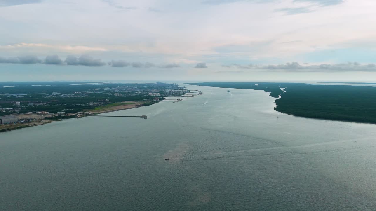 Aerial view of Westport in Selangor, Malaysia, stretching along the Straits of Malacca with calm waters, cargo terminals, distant vessels and coastal greenery under a cloudy sky. UHD.