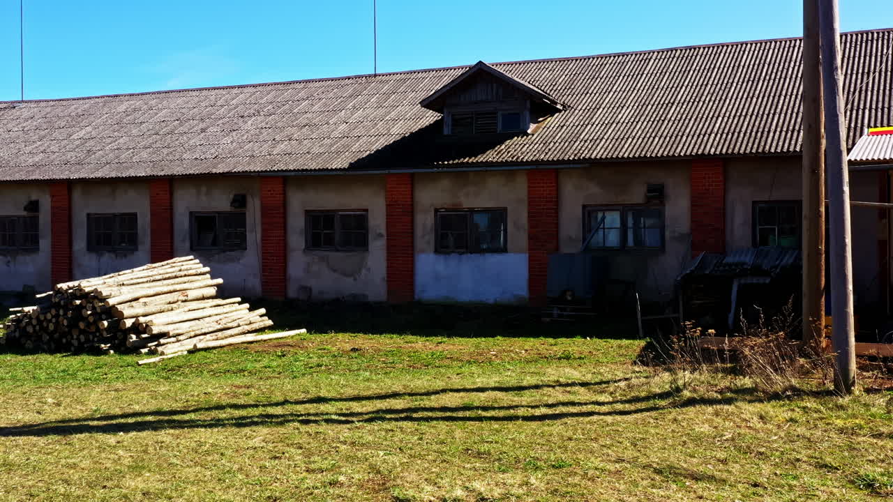 Long warehouse building with stacked wooden logs in open rural yard
