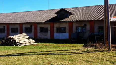 long warehouse building with stacked wooden logs in open rural yard