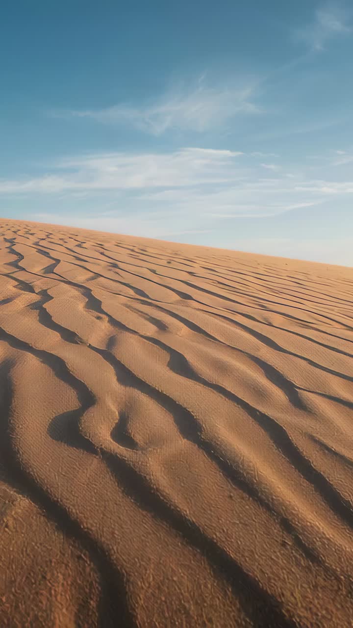 Video verticale: inquadratura che si allontana rivelando increspature di sabbia su una duna, la cresta, le ombre e i cirri