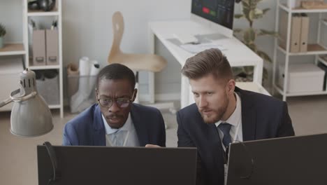 two male traders working on computers in office