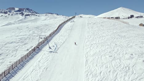 slow motion aerial view of a person with skis on the descent of farellones park with a ski lift on the side, chile