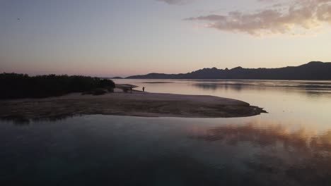 Aerial-Golden-Sunset-Over-Komodo-Islands-Hills-with-Silhouetted-Tourists-Walking-At-Dusk-on-a-Beach