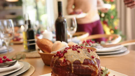 Happy-diverse-senior-male-and-female-friends-setting-dishes-on-christmas-dining-table,-slow-motion