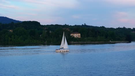 vista lateral de seguimiento de un pequeño velero en el lago maggiore navegando al atardecer