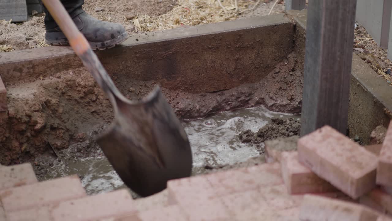 A construction worker mixes cement in a hole at a construction site, preparing the material for building or repair work.