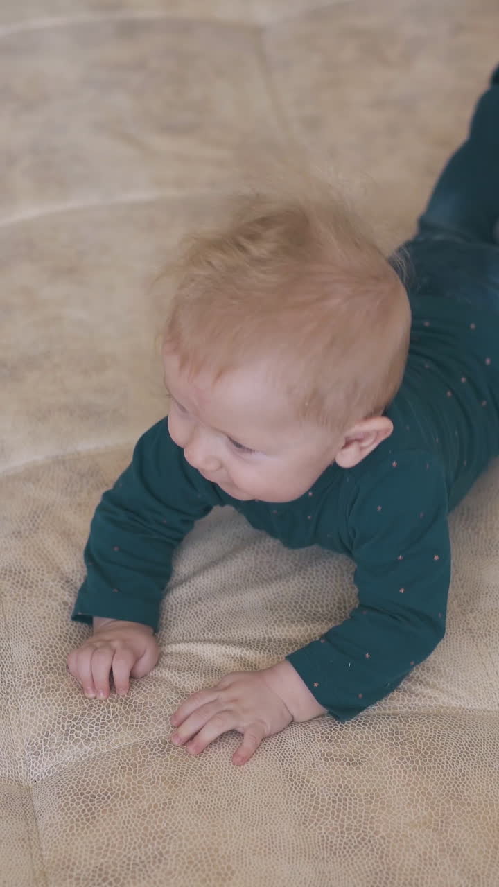funny small barefoot baby boy in jeans and green shirt rests on large soft bed in modern children room at home