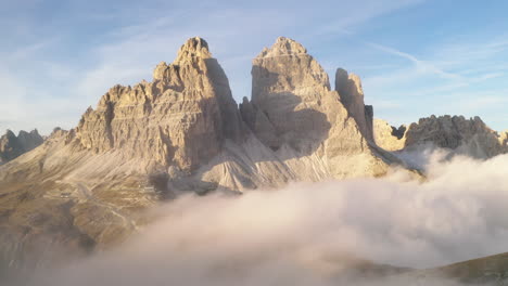 sunlit tre cime south tyrol mountains surrounded by creeping ethereal clouds at sunrise aerial orbiting view