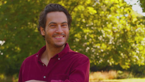 portrait of smiling casually dressed mature man leaning on fence on walk in countryside