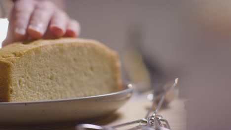 自宅のキッチンで作業台に焼きたてのケーキを切る男性の接写1