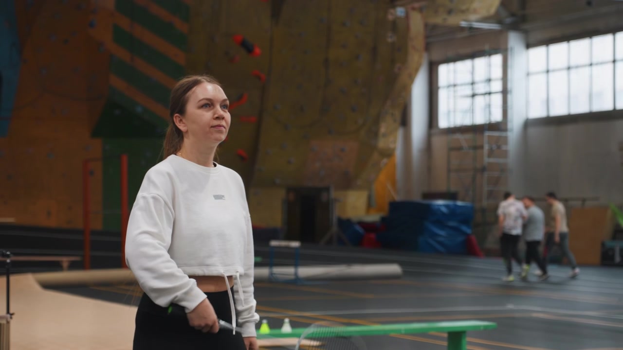 Brunette woman practicing badminton drills on indoor court, cropped white sweater and black leggings sequence shows grip adjustment, precise swing, controlled footwork, concentrated expression