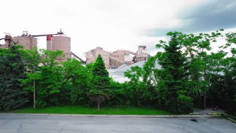 industrial buildings behind lush green trees and paved road