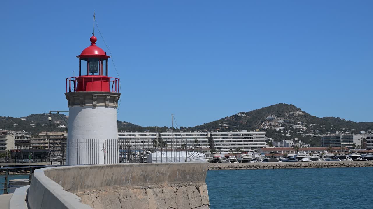La torre bianca dello storico faro si erge in modo prominente sul promontorio roccioso che si affaccia sul Mar Mediterraneo all'ingresso del porto in un pomeriggio di sole
