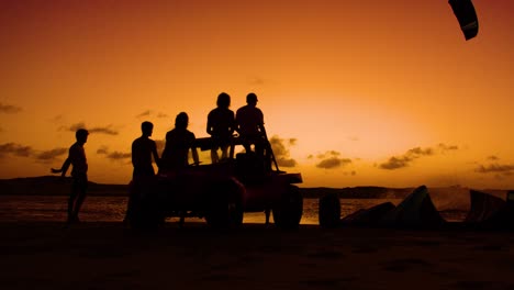 group silhouette of kitesurfers watching friend to a trick during sunset