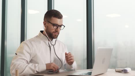 handsome male doctor sitting at the table with a stethoscope on the laptop screen