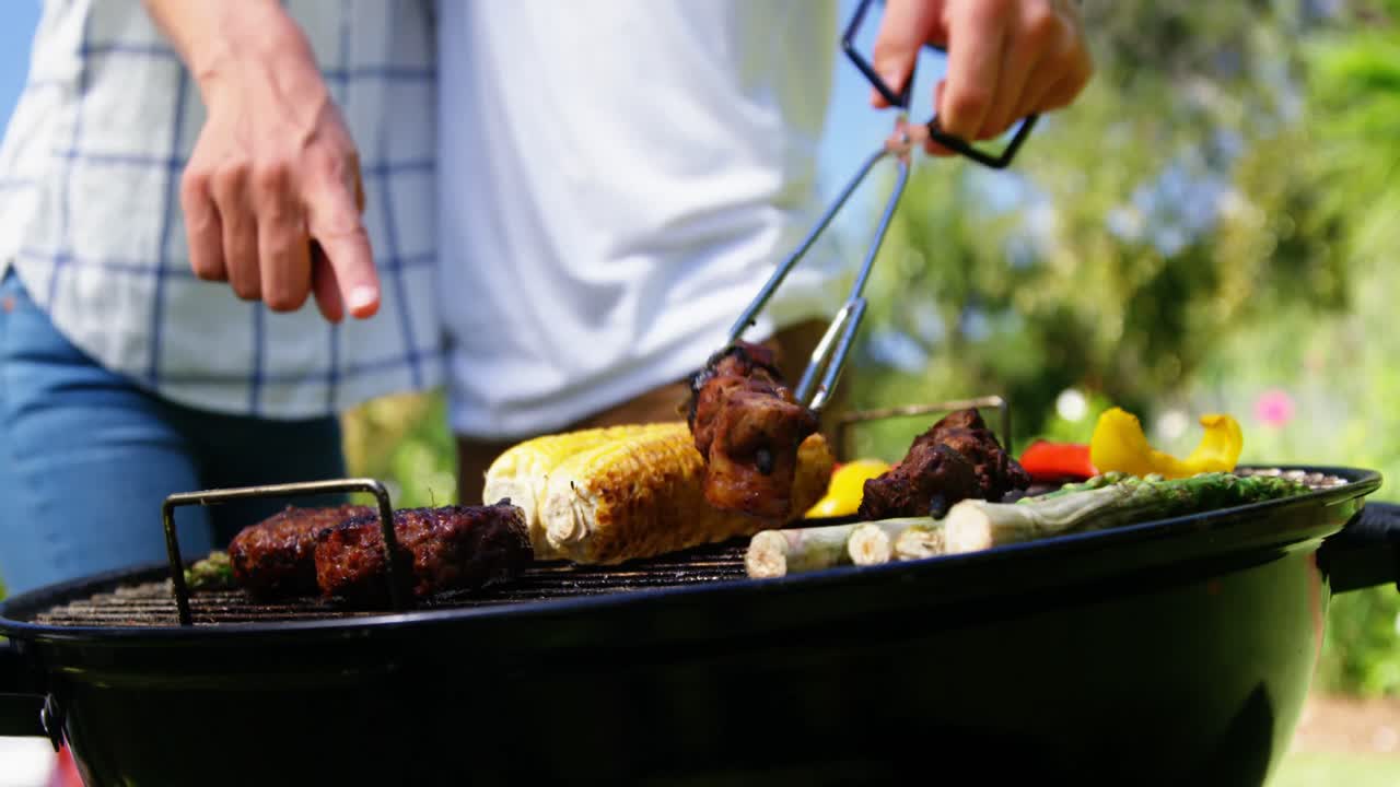 Coppia che griglia carne e verdure al barbecue