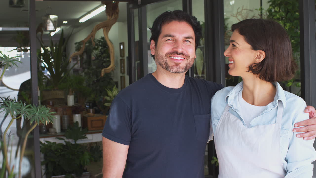 pareja propietaria de floristas de pie y abrazando en la puerta rodeada de plantas