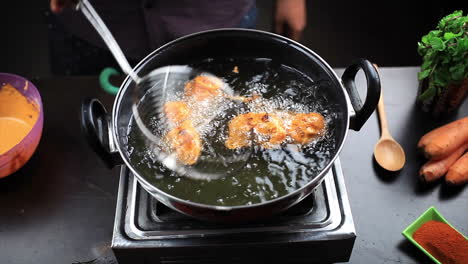 chef frying chicken lollipop in sizzling hot oil with a help of stainless steel deep fryer, cooking non vegetarian fast food at home