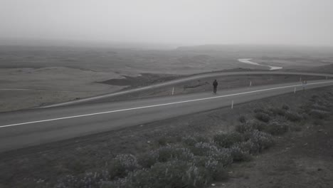 Drone-shots-of-skater-going-downhil-on-curvy-road-in-a-foggy,-dramatic-landscape-in-Iceland