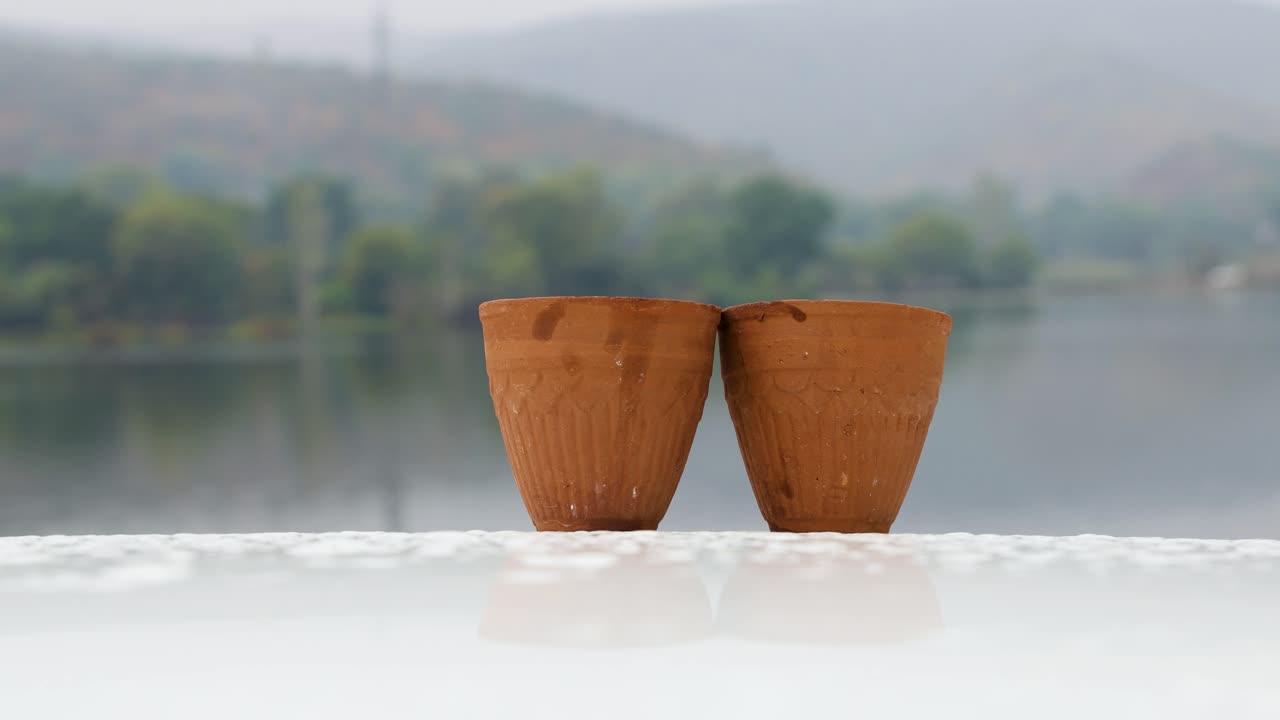 té caliente servido en una tradicional taza de arcilla de cerámica sin manijas con un paisaje borroso de lago de montaña