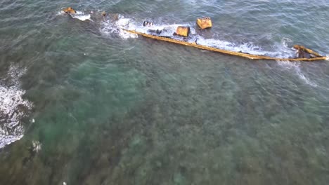 drone aerial moving backwards to reveal a ship wreck in the middle of the ocean